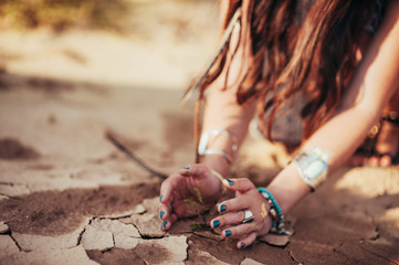 Hands of girl and little green plant on crack dry ground