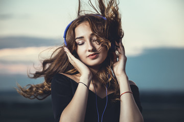 romantic portrait of a beautiful girl in headphones with flying hair from the wind, young woman...