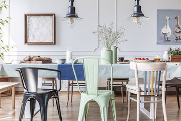 Colorful chairs at table in eclectic grey dining room interior with lamps and flowers. Real photo