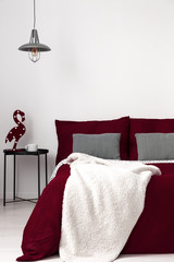 A bed dressed in burgundy organic cotton bedding and vanilla soft blanket in a modern bedroom...
