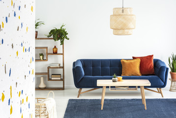 Lamp above wooden table in front of blue sofa with cushions in colorful living room interior. Real...