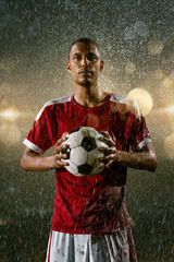 Soccer player on professional soccer night rain stadium. Dirty player in rain drops hold a football ball © Alex