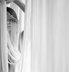 Portrait einer jungen attraktiven Frau mit unbedeckten Schultern, die mit den Händen dekorativ die Fäden eines Fadenvorhangs zieht, als schwarz weiß Bild mit Textfreiraum, Platz für Text.