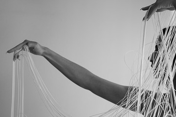 schwarz weiß Bild des Profils einer jungen attraktiven Frau mit unbedeckten Schultern, die mit den Händen dekorativ die weißen Fäden eines Fadenvorhangs zieht, Textfreiraum, Platz für Text.