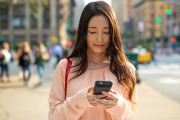 Asian woman in city walking using cell phone smile happy
