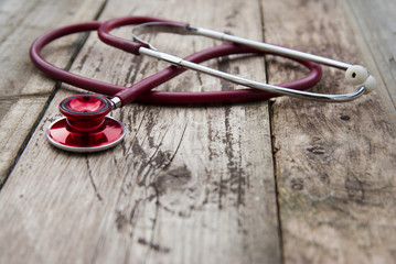 Medical red stethoscope isolated on rustic wooden background. Copy space. Healthcare and medicine.