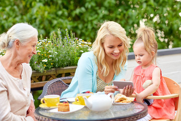 family, generation and technology concept - happy mother, daughter and grandmother using smartphone at cafe or restaurant terrace