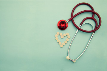 Red stethoscope with tablets, pills on blue background. Copy space. Medicine, heartbeast concept.