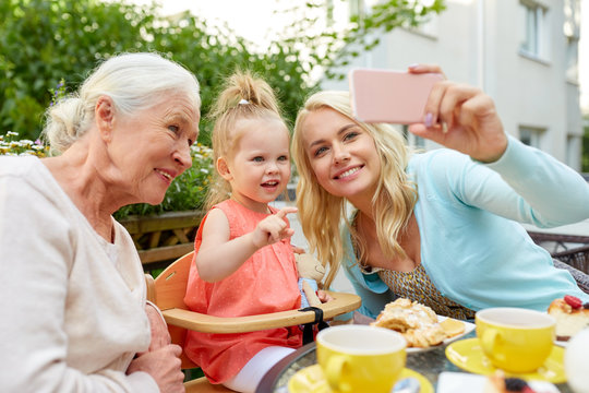 family, generation and people concept - happy mother, daughter and grandmother taking selfie by smartphone at cafe or restaurant terrace