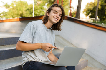 Handsome attractive oung skater guy sit in the park using laptop computer. © Drobot Dean