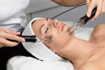 Beautiful woman receiving facial microcurrent treatment at spa salon. Beautician using electrical impulses for facial procedures.