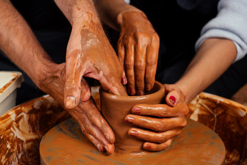 happy family on a creative joint vacation. romantic couple in love working together on potter wheel and sculpting clay pot,a bearded man and a young woman mold a vase in craft studio workshop.