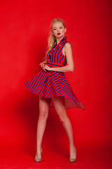 Model in red striped dress and stiletto heels posing on red background.