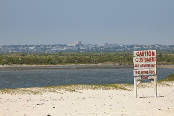 Tourist warning sign on Bojo Beach, Accra Ghana.  On a sandy beach with empty field and the city on...