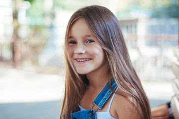 Little girl cheerful, laughs and sits on a bench in the park summer