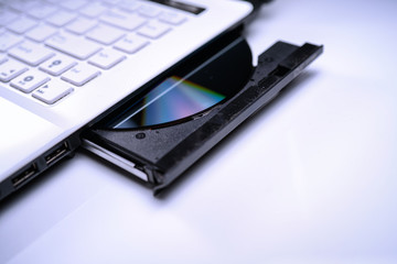 DVD Disk on the white Laptop DVD ROM Tray with a Man Hand. A Piracy conceptual image of burning data into DVD Disk