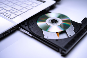DVD Disk on the white Laptop DVD ROM Tray with a Man Hand. A Piracy conceptual image of burning data into DVD Disk