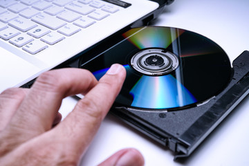 DVD Disk on the white Laptop DVD ROM Tray with a Man Hand. A Piracy conceptual image of burning data into DVD Disk