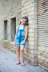 Fototapeta na wymiar Model little beautiful girl with long hair, street fashion near the wall on a summer