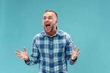 Fototapeta premium Screaming, hate, rage. Crying emotional angry man screaming on blue studio background. Emotional, young face. male half-length portrait. Human emotions, facial expression concept. Trendy colors