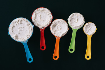 top view of a flour in a colorful measuring cup with FLOUR word on black background. concept of cooking,bakery and food ingredient