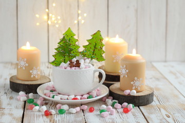 Christmas still life with sweets, marshmallows, candies in cup and candles on wooden table. Christmas and new year holidays background. winter festive season. Advent time.