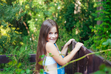 Little funny girl with long hair, portrait in a green park on a summer