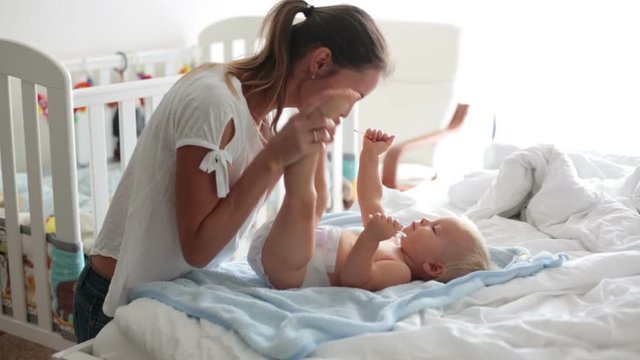 Young mom, changing baby diaper after bath in sunny bedroom