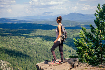 Young happy woman with backpack standing on a rock