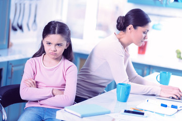 Obraz premium Feeling offended. Sad little girl sitting next to her busy mother with her arms crossed and feeling offended