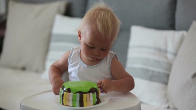 Little baby boy, celebrating his first birthday, having cake and ballons