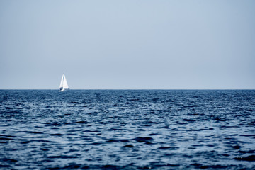 A view of the sea, a white yacht with sails and the sky.