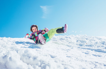 Happy little girl slides down from the snow slope