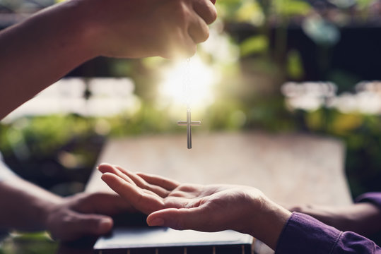 Christian hands of giving cross necklace to friend in summer. Christian and prayer concept.