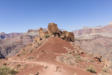 Beautiful rock boulders on a hill of red sand on a hiking trail down the Grand Canyon with a view of the famous rock formations on the background.