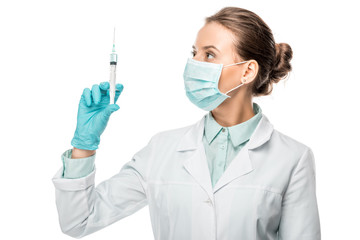 female doctor in medical mask looking at syringe isolated on white
