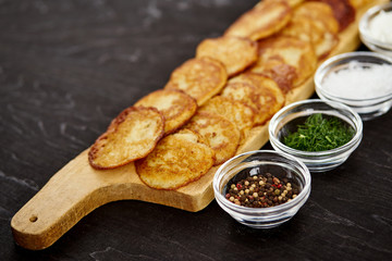 delicious potato pancakes and bowls with additions on an old wooden black table in the kitchen