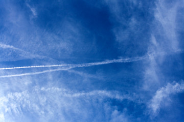 Footprints, white stripes from flying planes in the blue sky with clouds.