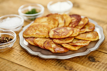 metal plate with delicious potato pancakes on an old wooden table with bowls full of additions in the kitchen