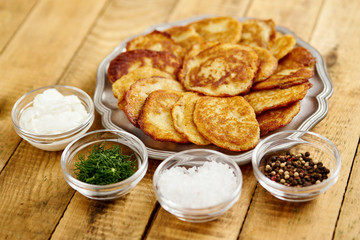 metal plate with delicious potato pancakes on an old wooden table with bowls full of additions in the kitchen