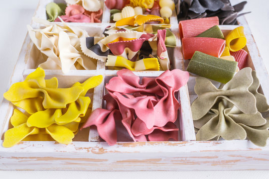 Mixed set of dry multi-colored Italian pasta on a white old wooden box. Background. Close up