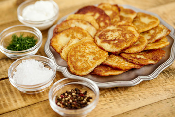metal plate with delicious potato pancakes on an old wooden table with bowls full of additions in the kitchen