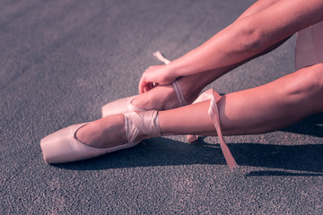 Minute to rest. Nice pleasant ballerina sitting on the ground while fastening her pointe shoes © Viacheslav Yakobchuk