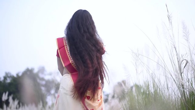 An Indian woman in saree with beautiful long and curly hair sways and moves her hair in a field, slow motion