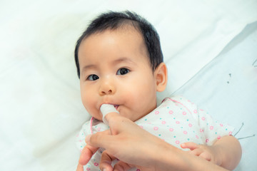 Mother use finger to clean asian baby tongue with clean gauze.