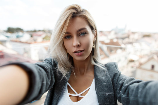 Beautiful stylish young woman in a vintage fashion coat is traveling and photographing on the roof of the city. Girl makes selfie