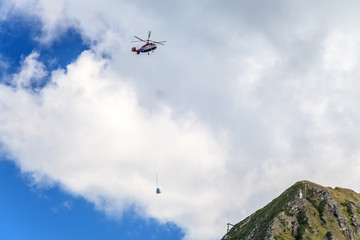 Helicopter in the air carrying gas cylinders on steel rope for maintaining avalanche control systems Gazex