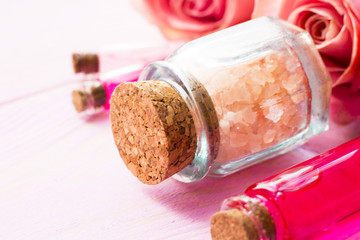 Spa and wellness setting with rose flower, sea salt, oil in a bottle on wooden white background