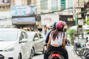 Fototapeta na wymiar Women in colorful helmets riding a bicycle down the streets of Hanoi, Vietnam. Street traffic and shops in the capital city.