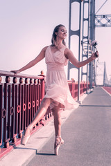 Symbol of beauty. Joyful professional ballerina dancing with a flower while touching the parapet